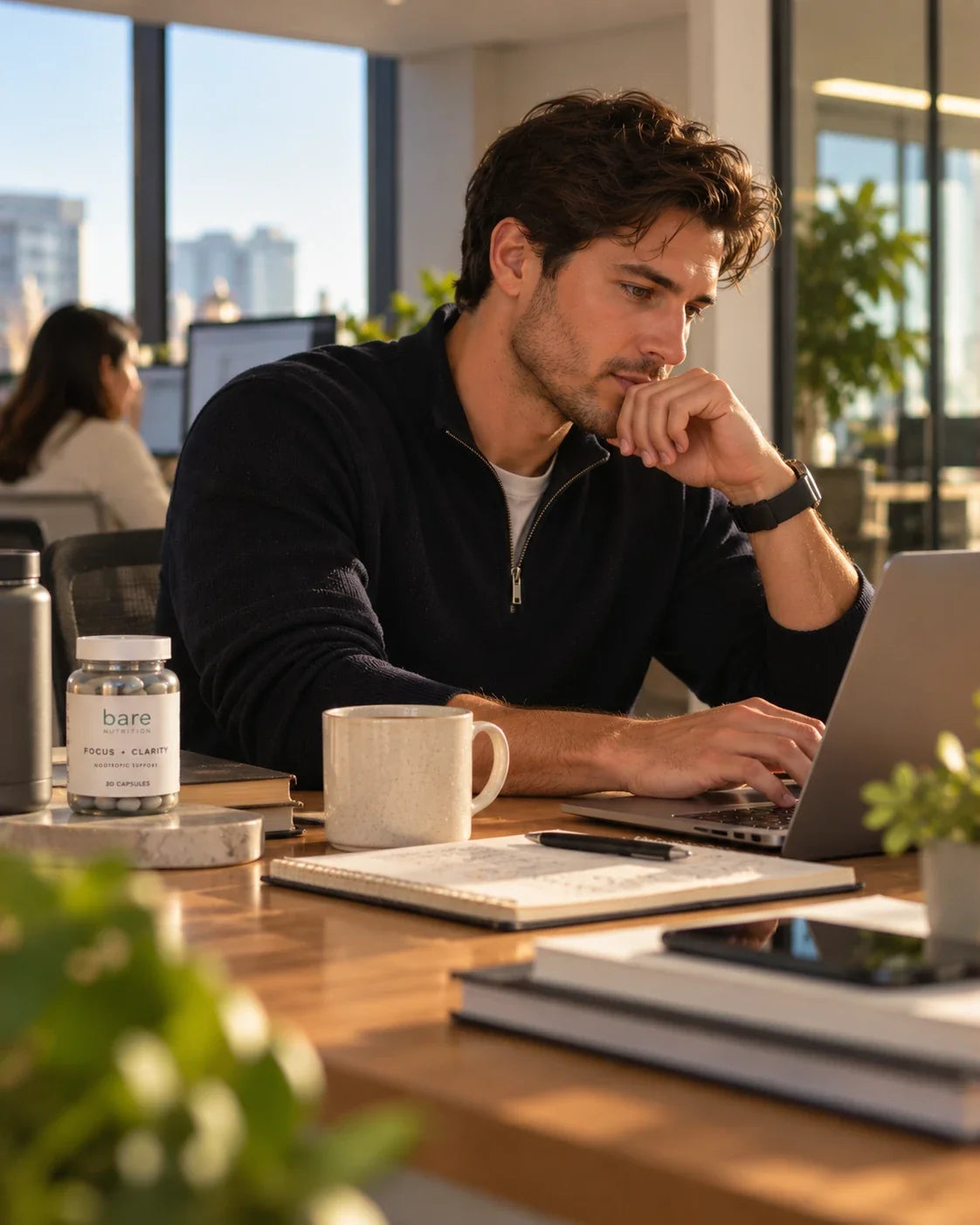 Man focused on his laptop at a sunny desk, with a jar of bare Focus + Clarity beside his coffee